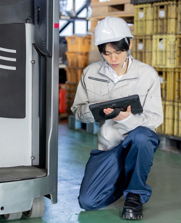 倉庫でフォークリフトをタブレットで点検する整備士