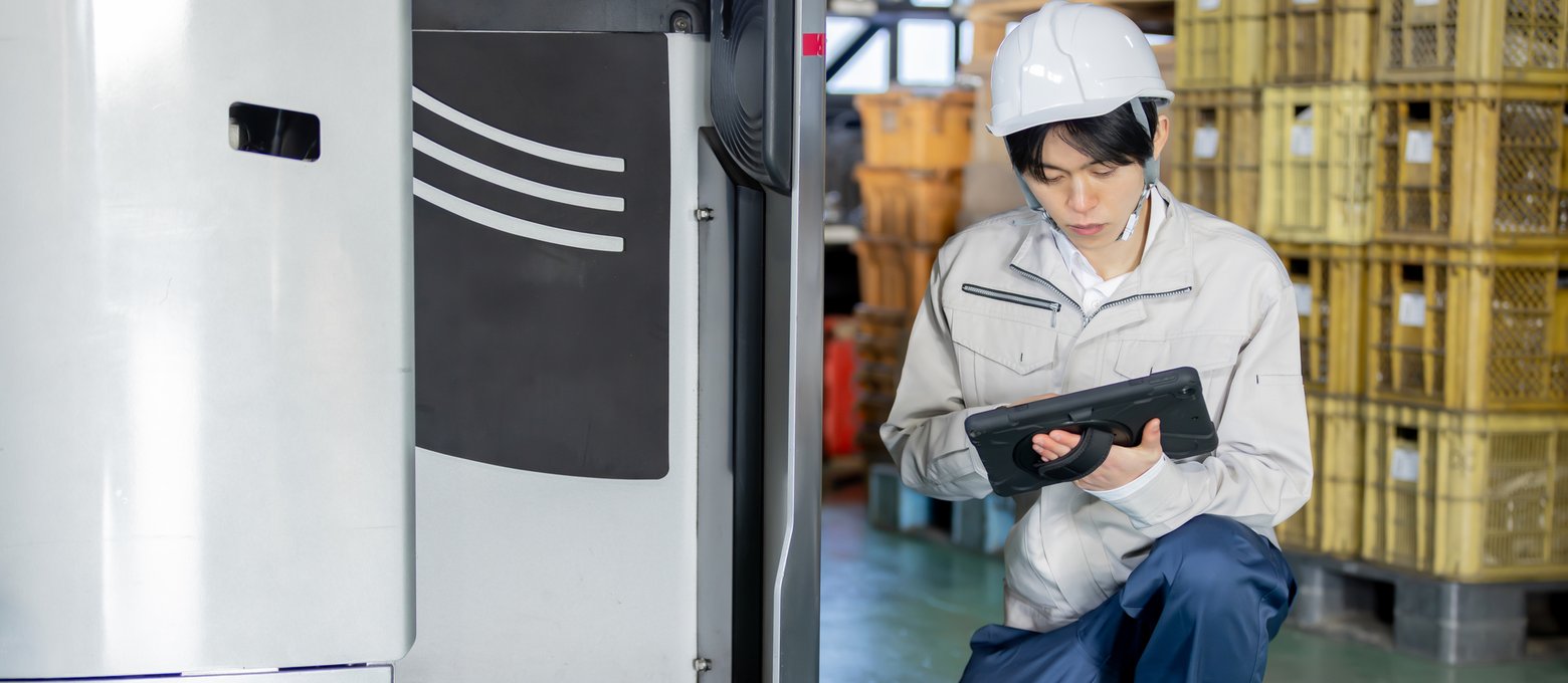 フォークリフトの横でタブレットを確認する整備士